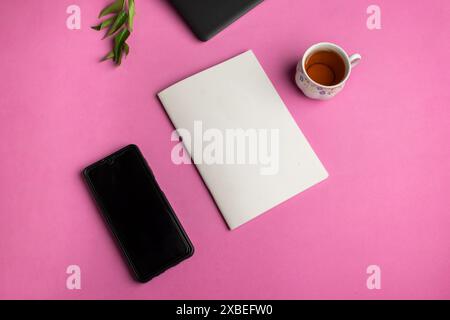 Draufsicht eines Buchmodells auf einem Bürotisch mit Laptop, Smartphone, Tasse und Blättern auf rosa Hintergrund Stockfoto