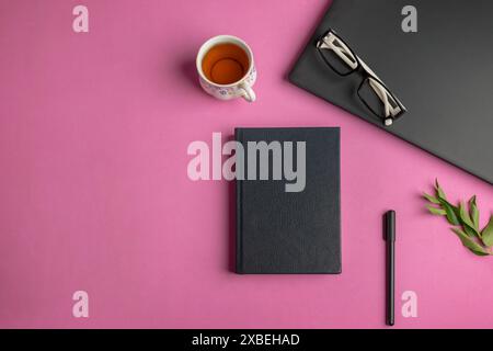 Draufsicht eines Buchmodells auf einem Bürotisch mit Laptop, Stift, Brille, Tasse und Blättern auf rosa Hintergrund Stockfoto