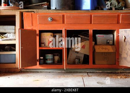 Ein alter Küchenschrank, der als Stauraum in einer Garage des Hauses genutzt wird, offene Türen zeigen Farbdosen, Leser verdauen Zeitschriften und Gartenarbeit-Bric-a-Brac Stockfoto