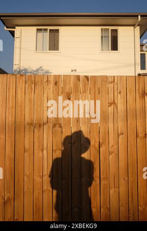 Schattenselfie an einem unbemalten Kiefernzaun vor einem hohen Vorstadthaus an einem hellen sonnigen Tag in Carina, Brisbane Stockfoto