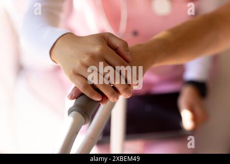 Pflegekraft hält Hände mit älteren asiatischen Frauen, die zu Hause Walker benutzen. Sie sind in heller, gemütlicher Wohnumgebung, was auf ein unterstützendes A hindeutet Stockfoto