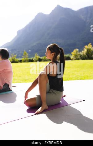 Asiatische Großmutter und birassische Enkelin üben gemeinsam Yoga an sonnigen Tagen. Sie sind im Freien mit malerischem Blick auf die Berge und üppigem Grün Stockfoto