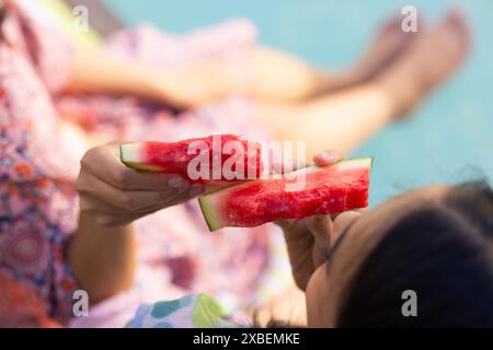 Zwei junge birassische Schwestern, die gemeinsam Wassermelonenscheiben genießen, zu Hause Stockfoto