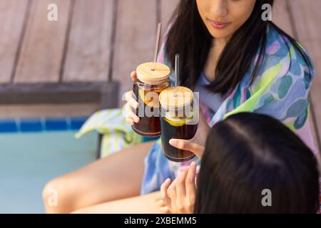 Zwei junge Schwestern, die gemeinsam am Pool trinken, zu Hause Stockfoto