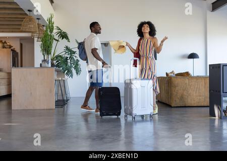 Ein vielseitiges Paar steht in einem modernen Ferienhaus mit Koffern und wirkt aufgeregt Stockfoto