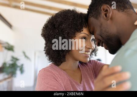 Eine junge Frau lächelt und umschließt ihren Partner in einem gemütlichen, gut beleuchteten Wohnzimmer Stockfoto