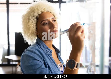 Junge Frau, die im Büro auf Glasplatte schreibt. Große Fenster und moderne Möbel im Business Office mit unverändertem Hintergrund Stockfoto