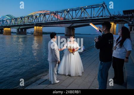 Harbin, Chinas Provinz Heilongjiang. Juni 2024. Ein Paar posiert für Hochzeitsfotos entlang des Songhua Flusses in Harbin, nordöstlicher chinesischer Provinz Heilongjiang, 4. Juni 2024. Quelle: Xie Jianfei/Xinhua/Alamy Live News Stockfoto