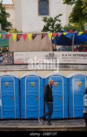 Besucher des jardim da graca während der beliebten Heiligen Festlichkeiten, spazieren in der Nähe von tragbaren Toiletten und farbenfrohen Dekorationen Stockfoto