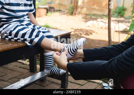 Eine Mutter, die sanft Socken auf ihrem Kleinkind-Sohn in der Bank legt, veranschaulicht das Konzept der Erziehung und Mutterschaft Stockfoto