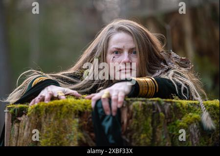 Eine Frau lehnt sich auf einen moosbedeckten Baumstamm in einem Wald. Geringe Tiefe von feld Stockfoto