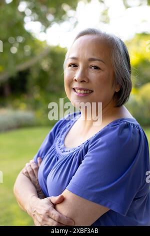 Asiatische Seniorin lächelt mit überkreuzten Armen, erscheint zufrieden und entspannt, zu Hause Stockfoto