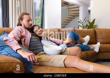 Eine junge Frau und ein junger Kaukasier entspannen sich auf einer Couch, die Popcorn teilt Stockfoto