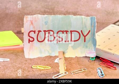 Geschäftskonzept. SUBVENTIONSWORT auf Papier in einer Wäschespine in einer Komposition mit Rechner, Aufklebern und verstreuten Büroklammern Stockfoto