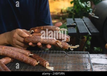 Ein Mann hält hausgemachte Würstchen, die aus Kollagendärmen hergestellt wurden und gepökelt wurden. Sie werden mit der Kaltrauchtechnik gekocht Stockfoto