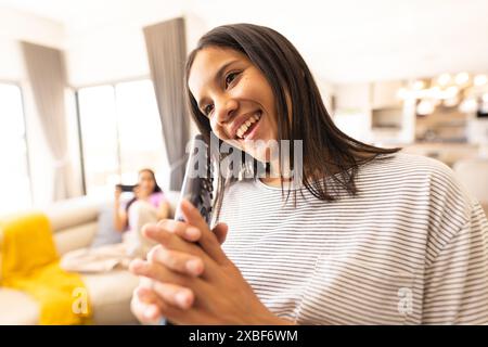 Zwei junge birassische Schwestern hängen herum, eine hält Fernbedienung und lächelt, zu Hause Stockfoto