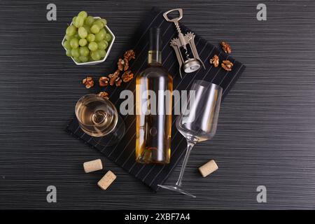 Flügelkorkenzieher, Flasche Wein, Gläser, Korken, Walnüsse und Trauben auf schwarzem Tisch, Blick von oben Stockfoto