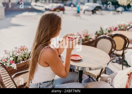 Frau sitzt an einem Tisch mit einer Tasse Kaffee vor sich. Die Szene spielt in einem Café mit Stühlen und Topfpflanzen Stockfoto