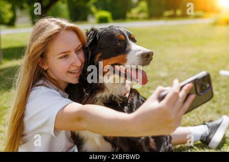 Eine Frau fängt freudig einen Moment ein, indem sie ein Selfie mit ihrem geliebten Hund auf dem Gras macht und beide eine glückliche und ehrliche Geste teilen Stockfoto