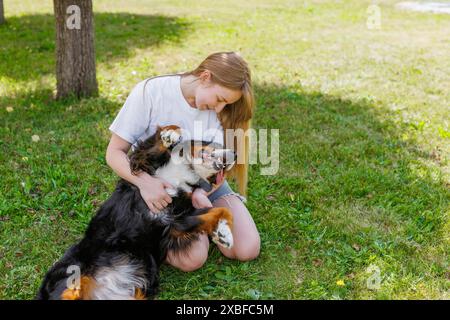 Eine Frau kniet auf dem Gras und streichelt ihren Hund in einem sonnigen Park mit üppigem Grün herum Stockfoto