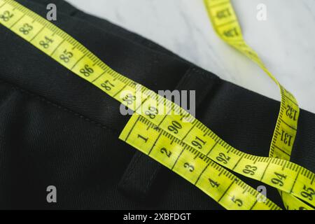 Eine schwarze Hose wird mit einem gelben Maßband gemessen. Das Konzept des gesunden Lebens Stockfoto
