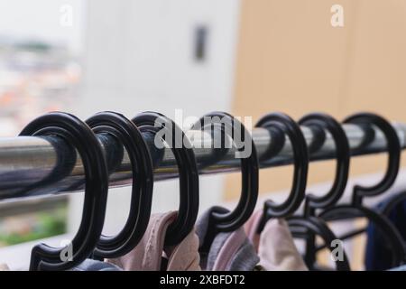 Eine Reihe von Kleidern hängt an einer Wäscheleine. Die Kleidung hängt an einem Metallstab mit schwarzen Haken, um die Sonne zu trocknen Stockfoto