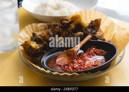 Sambal, traditionelle indonesische Chilli-Sauce, serviert mit traditionellem gebratenem Huhn mit Kurkuma und dampfendem heißem Reis Stockfoto
