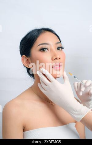 Schöne asiatische Frau mit Hochsteckfrisur, die sich einer Gesichtsfüller-Injektion unterzieht Stockfoto