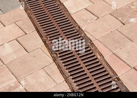 Eine Nahaufnahme eines Mannlochdeckels in einem gemauerten Bürgersteig zeigt komplizierte Muster auf der Metalloberfläche, die dem umgebenden Mauerwerk gegenübersteht Stockfoto