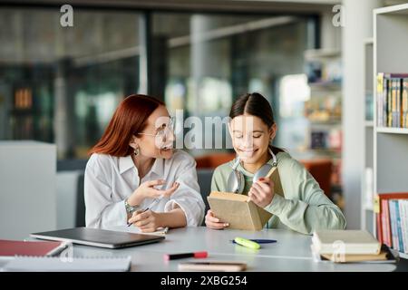 Eine rothaarige Frau unterrichtet ein Teenager-Mädchen in einer Bibliothek, vertieft in After-School-Unterricht mit einem Laptop. Stockfoto