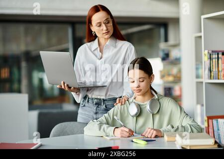 Eine rothaarige Frau unterrichtet ein Teenager-Mädchen an einem Schreibtisch mit einem Laptop und nimmt an After-School-Unterricht Teil. Stockfoto