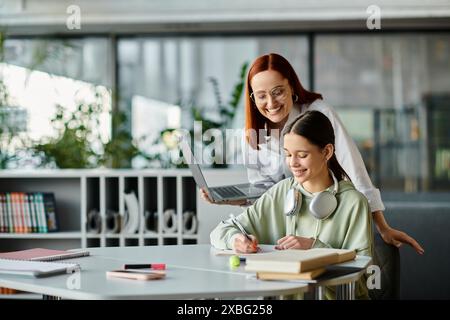 Eine rothaarige Frau unterrichtet ein Teenager-Mädchen an einem Schreibtisch, beide konzentrieren sich während einer Nachhilfesitzung auf einen Laptop. Stockfoto