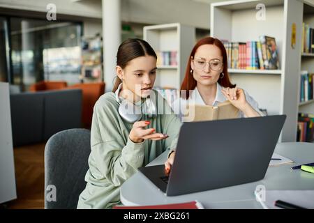 Eine rothaarige Frau unterrichtet ein Teenager-Mädchen an einem Tisch, beide konzentrieren sich während einer Nachschulstunde auf einen Laptop. Stockfoto