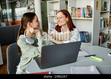 Eine Tutorin, eine rothaarige Frau, unterrichtet ein Teenager-Mädchen während einer Nachschulstunde, beide sind daran beteiligt, gemeinsam mit einem Laptop zu lernen. Stockfoto