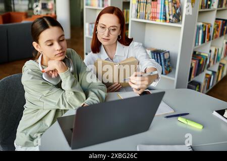 Eine Tutorin, eine rothaarige Frau, unterrichtet ein Teenager nach der Schule, indem sie einen Laptop benutzt, um den Lernprozess zu erleichtern. Stockfoto