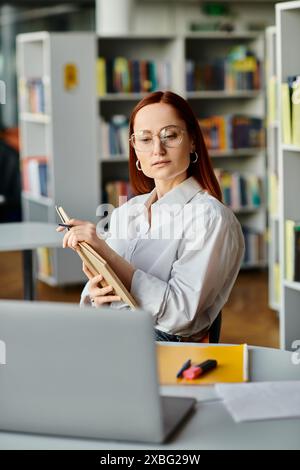 Eine rothaarige Tutorin unterrichtet online aus einer Bibliothek und benutzt einen Laptop für den After-School-Unterricht. Stockfoto