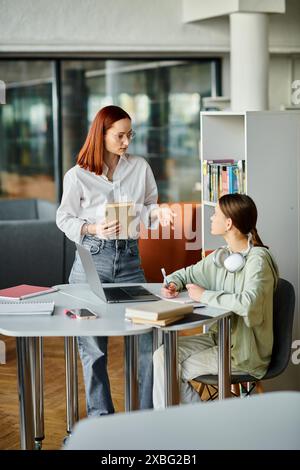 Eine rothaarige Frau unterrichtet ein Teenager-Mädchen an einem Tisch in einem Büro und benutzt einen Laptop für moderne Bildung nach der Schule. Stockfoto