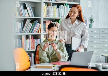 Ein rothaariger Tutor unterrichtet ein Teenager nach der Schule, sitzt mit einem Laptop an einem Schreibtisch in einer modernen Büroumgebung. Stockfoto