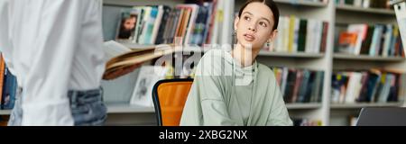 Ein Tutor mit rotem Haar unterrichtet ein Teenager an einem Schreibtisch in einer Bibliothek und benutzt einen Laptop für moderne Unterrichtsstunden. Stockfoto