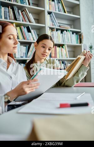 Ein rothaariger Tutor führt ein Teenager bei einer Nachschulstunde an einem Büchertisch und teilt mit Hilfe eines Laptops Wissen. Stockfoto