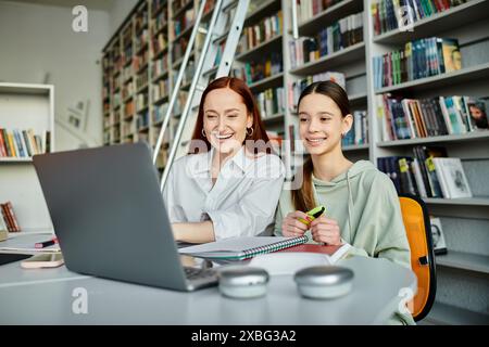 Die Redhead-Tutorin unterrichtet ein Teenager an einem Bibliothekstisch mit Laptops und nimmt an After-School-Unterricht Teil. Stockfoto