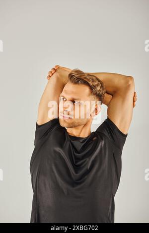 Ein junger Sportler in einem schwarzen T-Shirt posiert vor grauem Hintergrund in einem Studio. Stockfoto