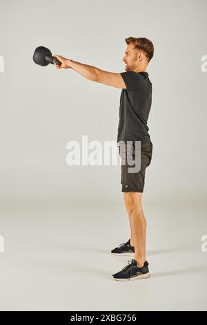 Junger Sportler in aktiver Kleidung, der Stärke und Entschlossenheit mit Kettlebell auf weißem Hintergrund zeigt. Stockfoto