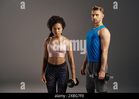 Multikulturelle Paare in Activewear schlagen mit Kurzhanteln vor grauem Studiohintergrund auf. Stockfoto