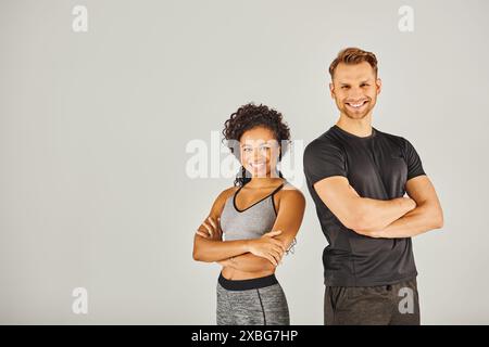 Ein junges, interrassisches Sportpaar, das aktive Kleidung trägt und zusammen in einem Studio vor grauem Hintergrund posiert. Stockfoto