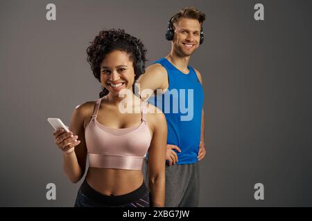 Ein junges, multikulturelles Paar steht zusammen, hält ein Handy und teilt einen Moment der Verbindung auf grauem Hintergrund. Stockfoto