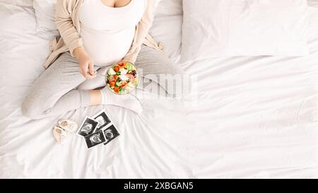 Frau, die auf dem Bett sitzt und eine Essensplatte hält, Blick von oben Stockfoto
