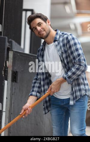 Männlicher Arbeiter, der den Boden in Stallungen reinigt Stockfoto