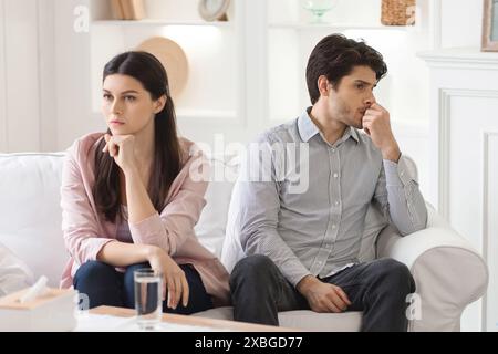 Ein junges Paar sitzt auf dem Sofa im Wohnzimmer und sieht verstört aus Stockfoto