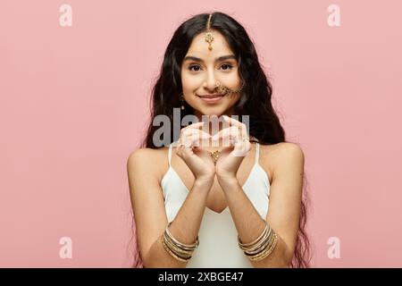indische Frau, die Herzsymbol mit Händen auf leuchtendem rosa Hintergrund bildet. Stockfoto
